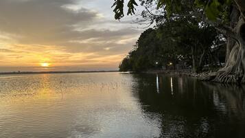 A calm river at sunset with trees and a distant shoreline.