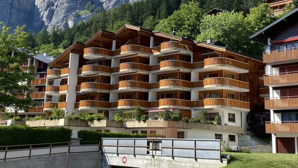 Un hotel a più piani con balconi in legno, con le montagne sullo sfondo.
