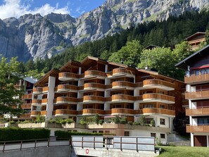 Un hôtel à plusieurs étages, doté de balcons en bois, qui se dresse sur un fond de paysage montagneux.
