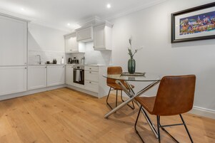 Una cocina moderna con armarios blancos, una mesa de comedor de vidrio y un jarrón en la pared.