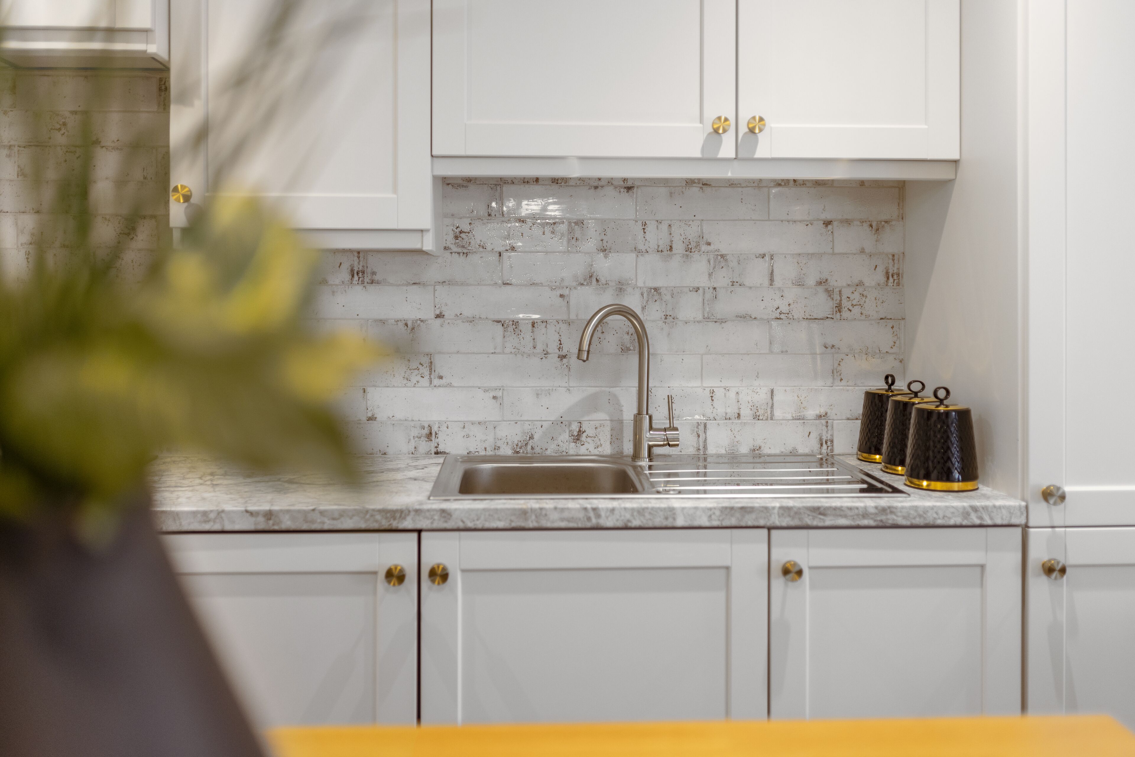A kitchen with white cabinets, a stainless steel sink, and a tiled backsplash.