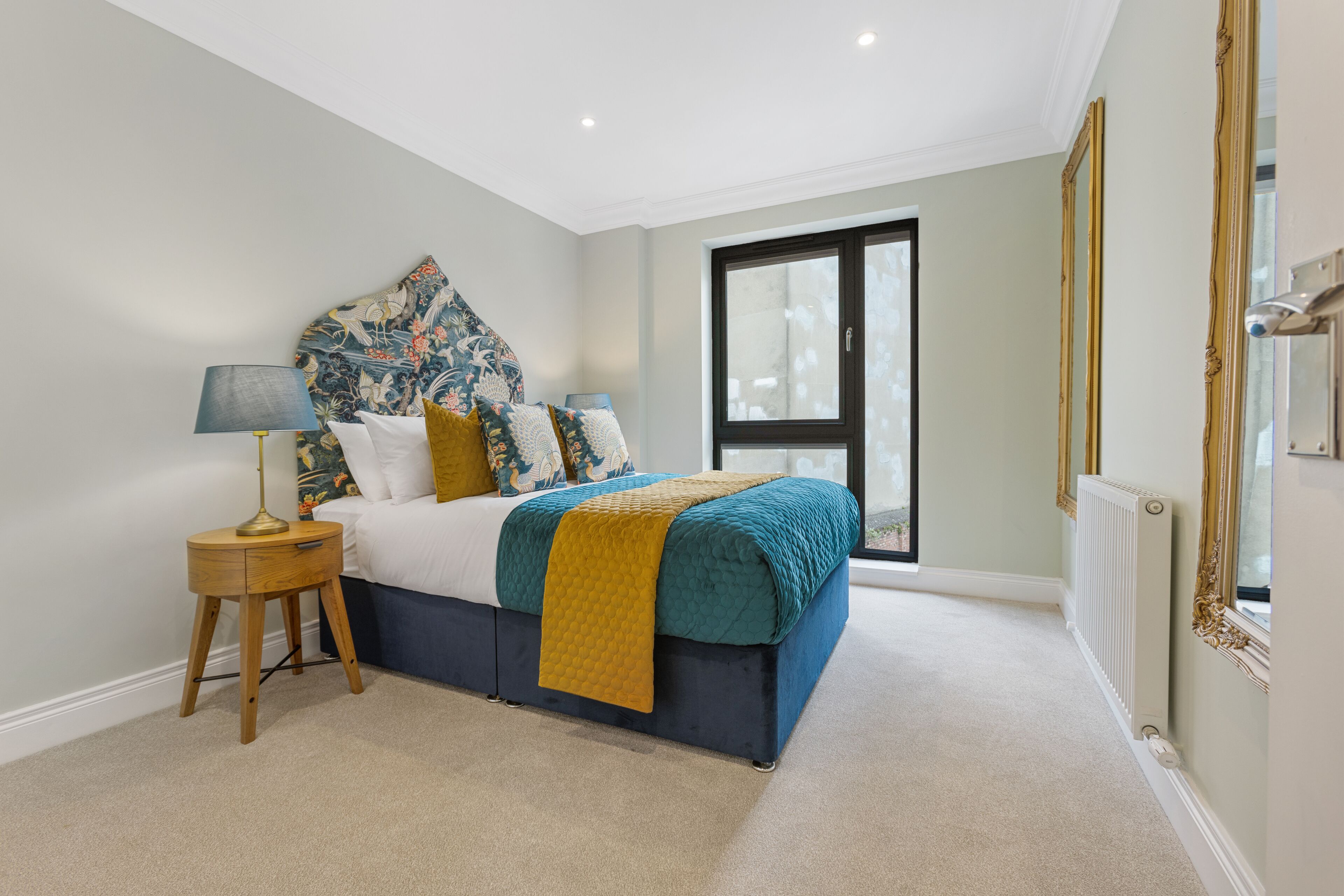 A bedroom with a bed, a nightstand, a window, and a radiator.
