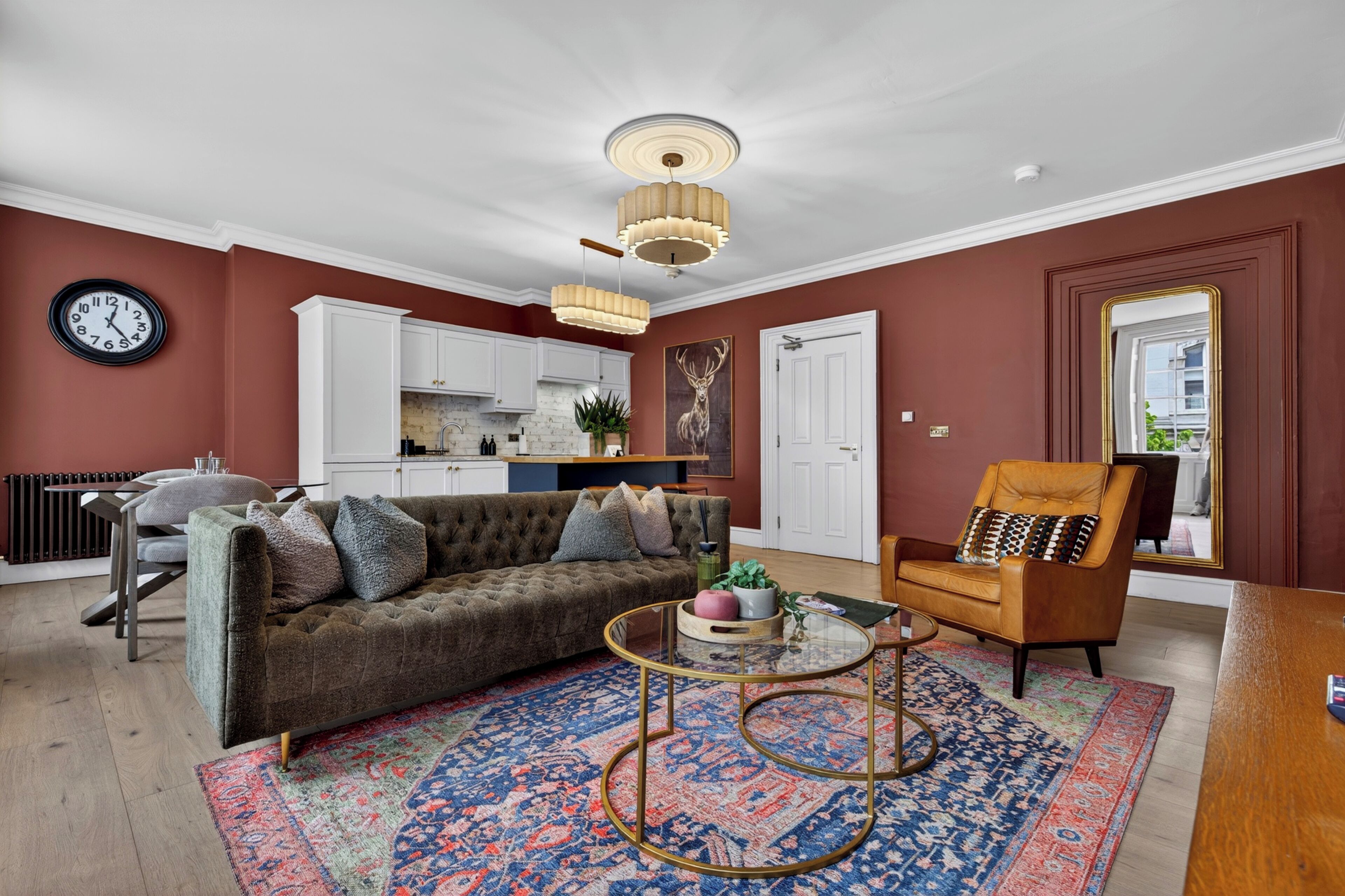 A living room with a sofa, coffee table, and a chair. There is a kitchen in the background with white cabinets and a dining area with a table and chairs.