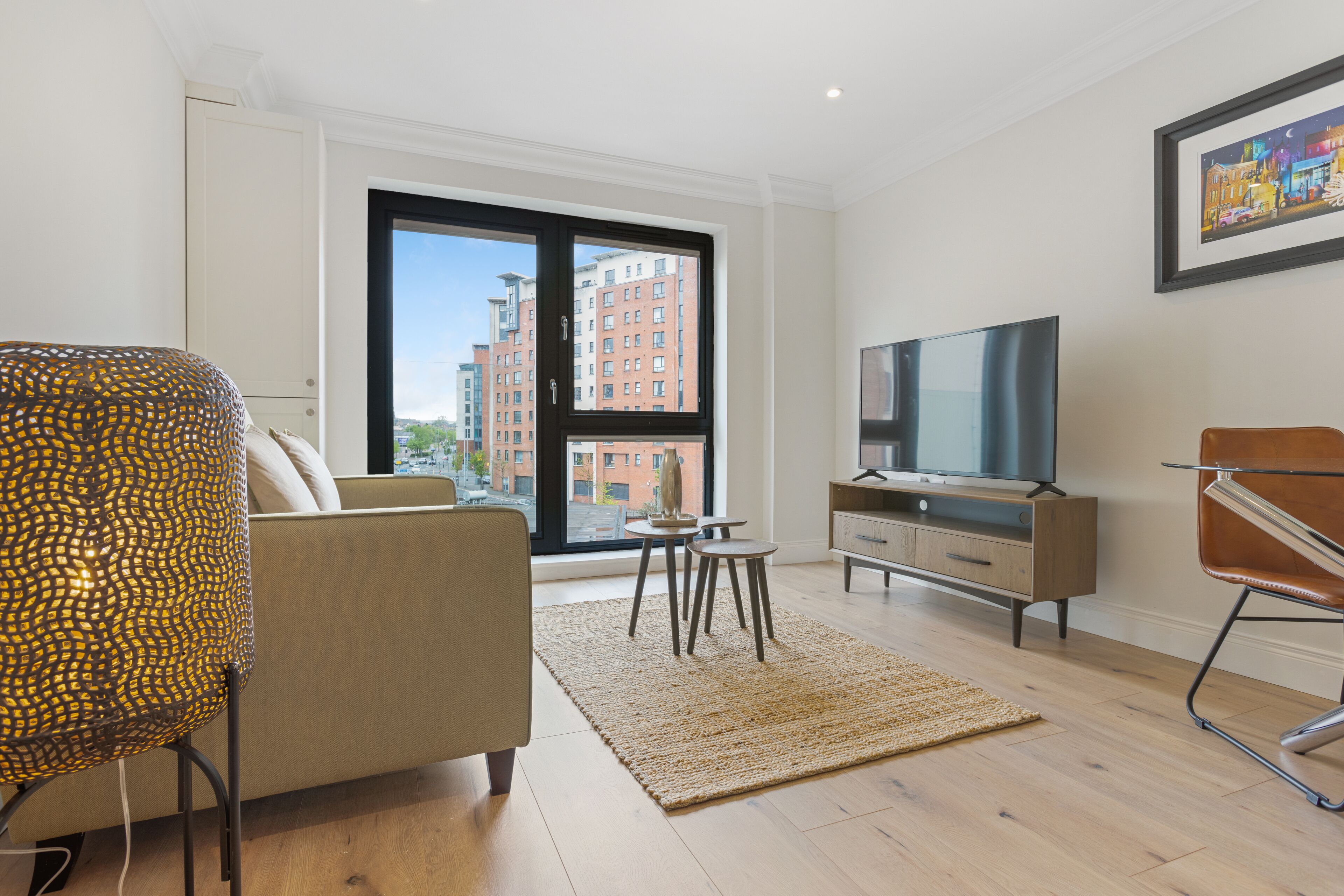A modern living room with a sofa, a TV, a coffee table, and a large window with a city view.