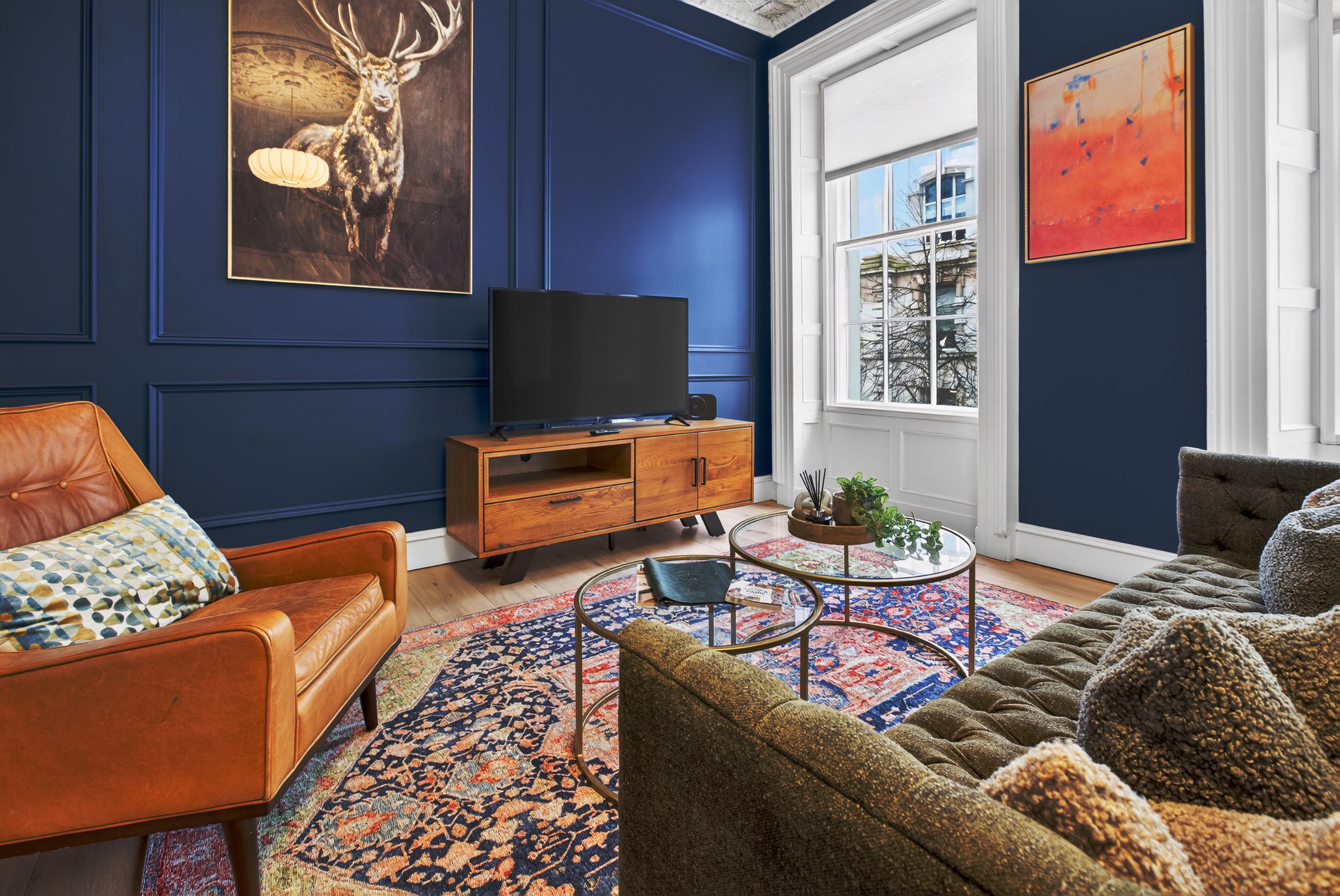 A living room with a leather sofa, a television on a wooden cabinet, a patterned rug, and artwork on the walls.