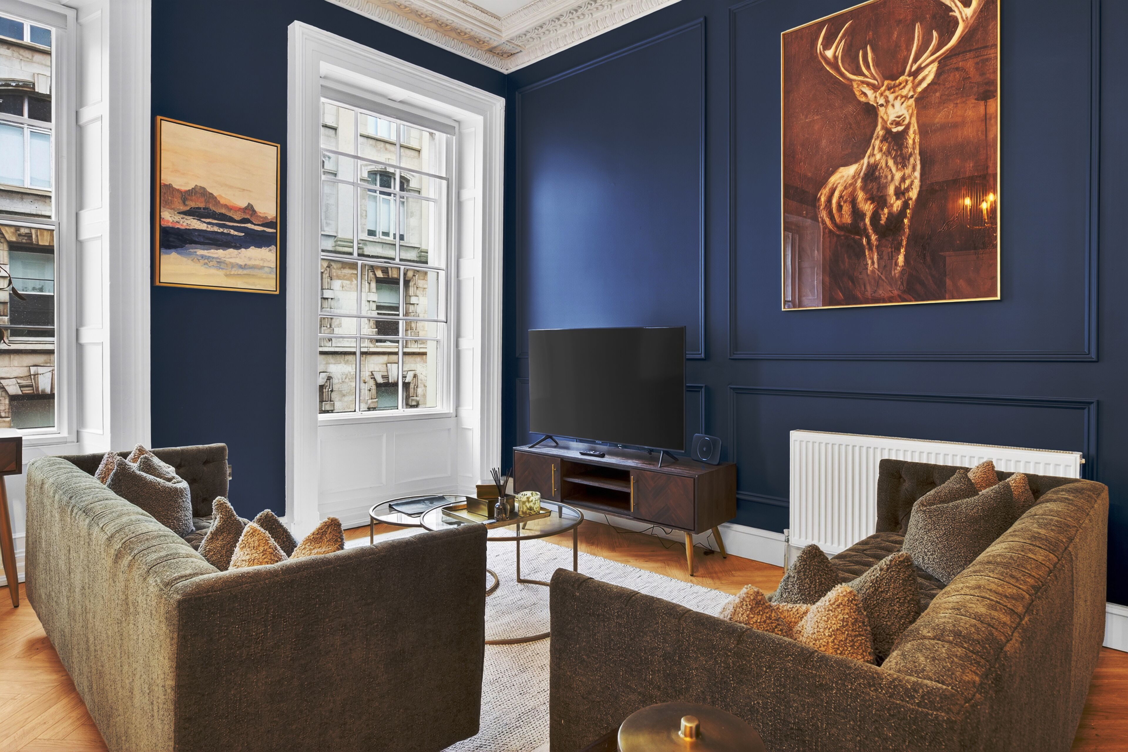 A living room with a large TV, two sofas, a fireplace, and a mounted deer painting.