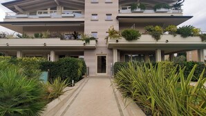 A modern multi-story building with a central entrance, balconies with plants, and a paved walkway. - Il Coccodrillo By Case al Lago (Sirmione)