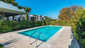 A rectangular swimming pool with metal ladders, surrounded by a tiled deck and lush greenery. - Il Coccodrillo By Case al Lago (Sirmione)