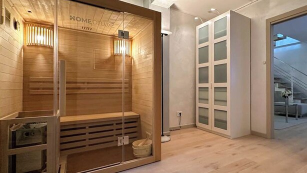 A sauna room with wooden benches and glass doors, a small bucket, and a wall-mounted heater. - Il Coccodrillo By Case al Lago (Sirmione)