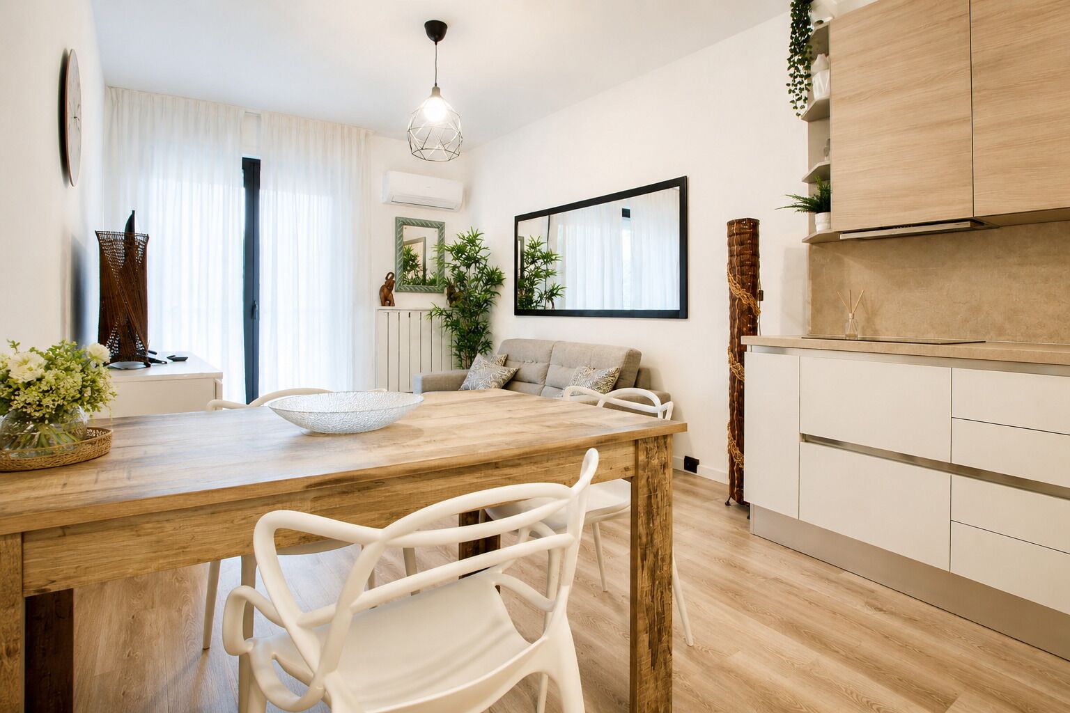 A modern kitchen with a wooden dining table, white chairs, and a hanging light fixture.