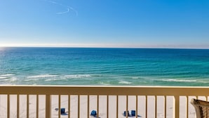 A beach view from a balcony with a railing, featuring a clear sky and calm sea.