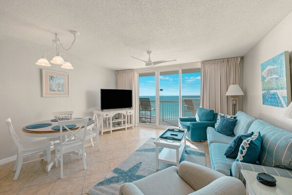A spacious living room with a balcony, a dining area, and a TV. - Pelican Beach 0805 1 Bedroom Condo by Pelican Beach Management (Destin)