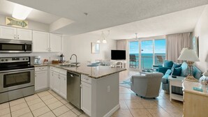 A spacious kitchen with a central island, a dining area, and a living room with a view of the ocean.