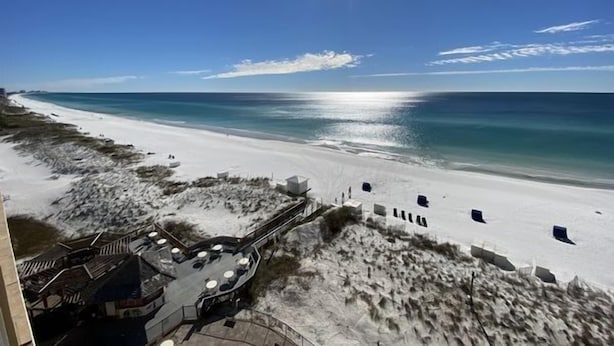 A beach view with a clear sky, a sandy beach, and a building with outdoor seating.