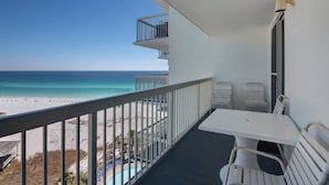A balcony with a view of the beach, a pool, and a table with chairs. - Pelican Beach 1014 2 Bedroom Condo by Pelican Beach Management (Destin)