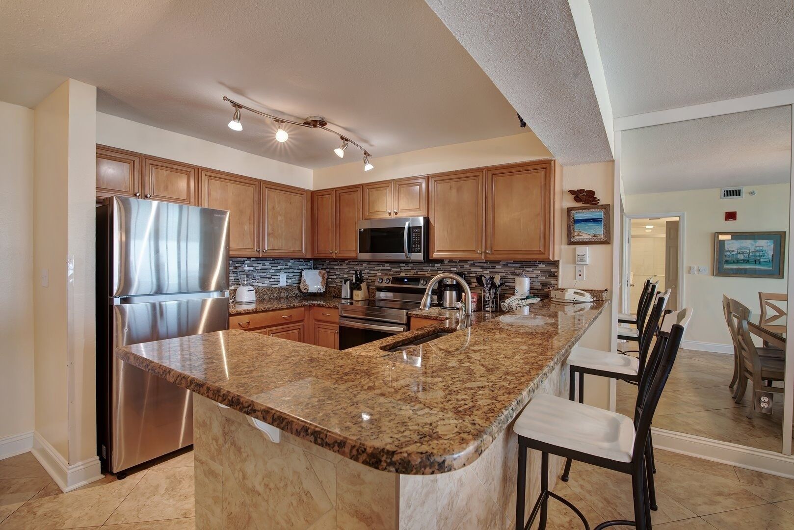A modern kitchen with granite countertops, stainless steel appliances, wooden cabinets, and a dining area with chairs.