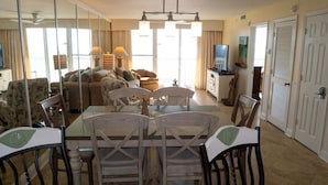 A dining area with a glass table, wooden chairs, and a ceiling fan. - Pelican Beach 1014 2 Bedroom Condo by Pelican Beach Management (Destin)