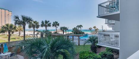 A resort balcony with a view of a pool, palm trees, and a beach.