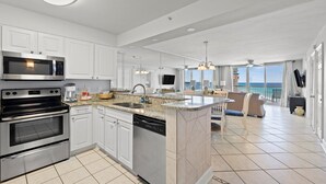 A modern kitchen with a central island, stainless steel appliances, and a view to the living area. - Pelican Beach 1414 2 Bedroom Condo by Pelican Beach Management (Destin)
