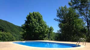 Piscina com deck revestido, rodeada por árvores e uma paisagem montanhosa.