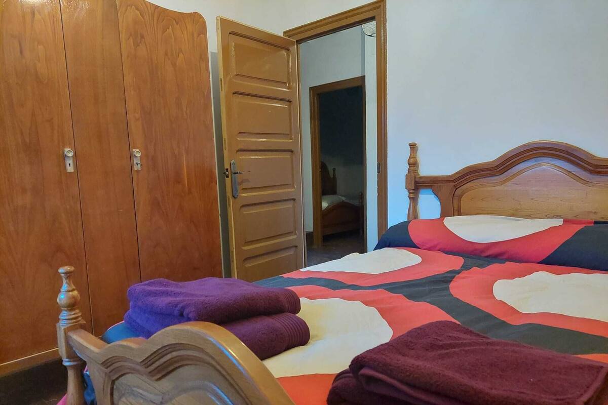 Een slaapkamer met een houten bedframe, een grote kledingkast en een deur naar een andere kamer.