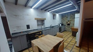Cozinha compacta com mesa e cadeiras de madeira, forno embutido e parede de pedra ao fundo.