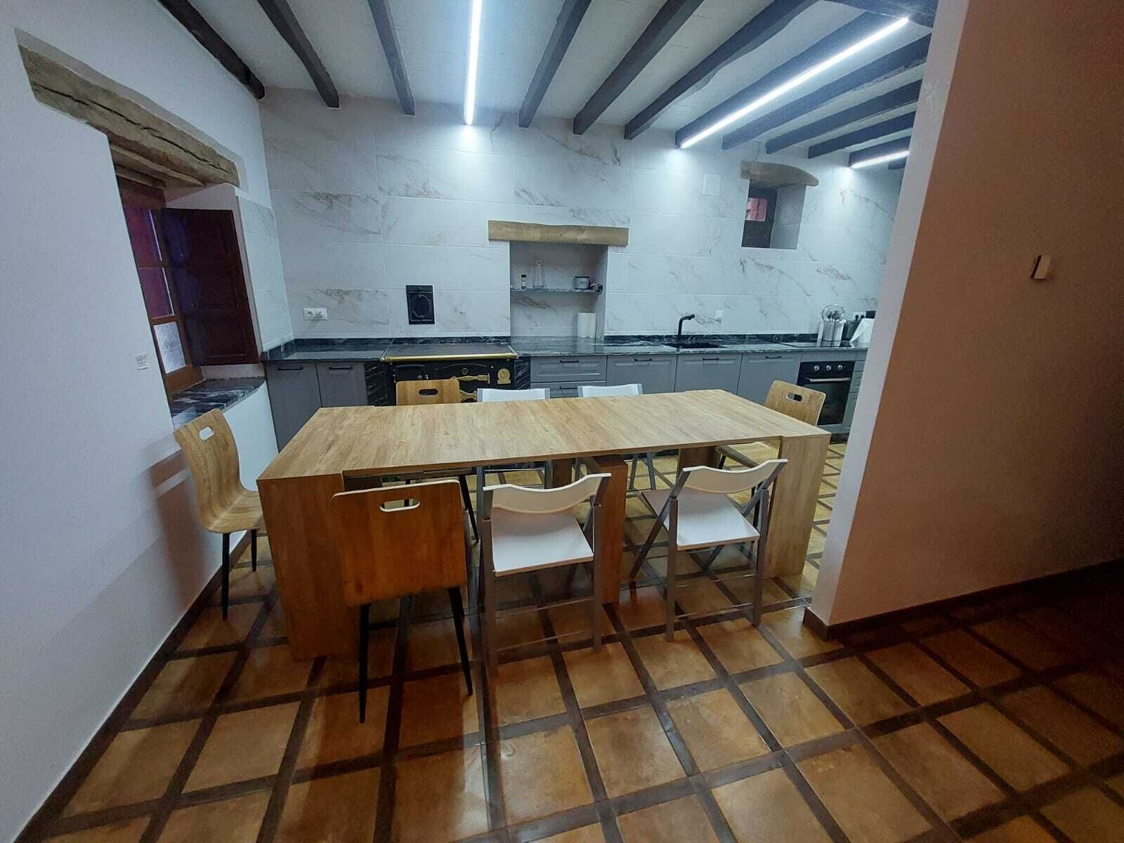 A compact kitchen with a wooden table and chairs, a built-in oven, and a tiled backsplash.