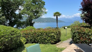 Un jardin offrant une vue sur un lac et des montagnes. On y trouve des chaises vertes et une table.