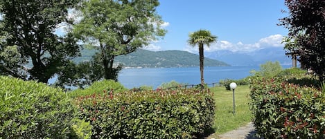 A garden with a view of a lake and mountains. There are green chairs and a table.