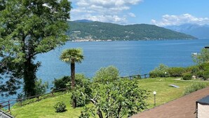 Une vue sur le lac, avec un grand arbre, un palmier et une zone herbeuse délimitée par une clôture.