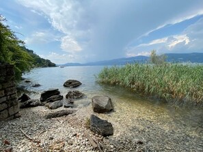 A rocky shoreline with clear water, a distant boat, and a view of mountains in the background.