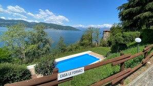 Vue d'un espace piscine avec une enseigne indiquant « CASA LE FORNACI » et un paysage pittoresque en arrière-plan, composé d'un lac et de montagnes.