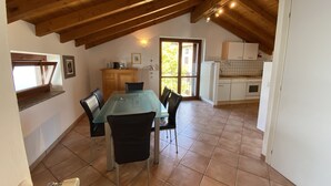 A dining area with a glass table and chairs, a wooden ceiling, and a kitchen in the background. - Gemütliche 3 Zimmer Fewo mit Traumblick (Leggiuno)
