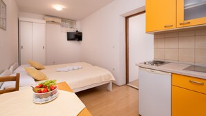 A bedroom with a bed, bedside table, and a small kitchen area with a sink and cabinets.