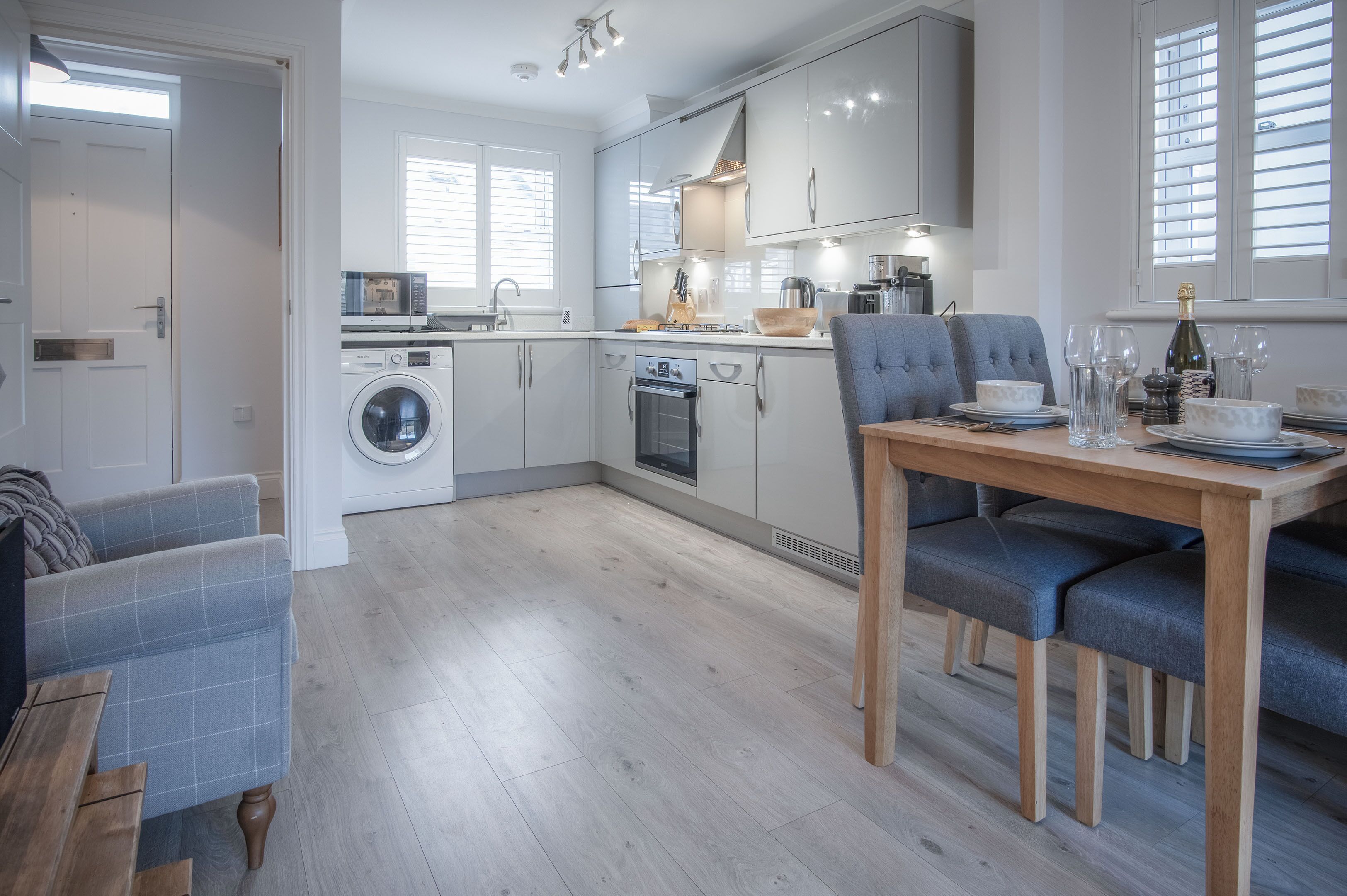 A modern kitchen with built-in appliances, a dining area with a wooden table and blue chairs, and a laundry area with a washing machine.
