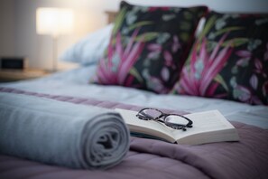 Una cama bien tendida con un edredón enrollado, un libro y un par de gafas encima.