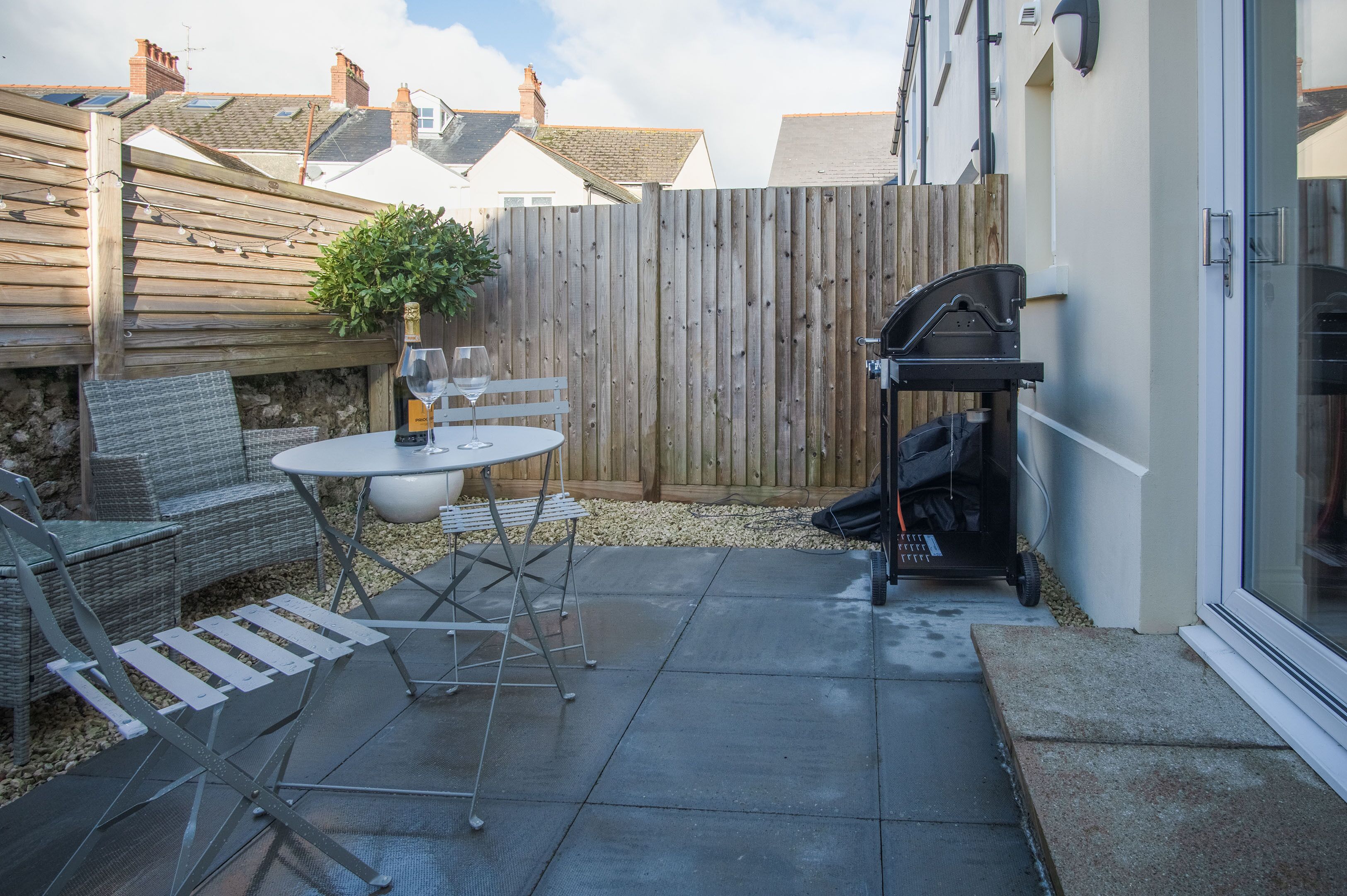 A patio with a table and chairs, a barbecue grill, and a wooden fence.