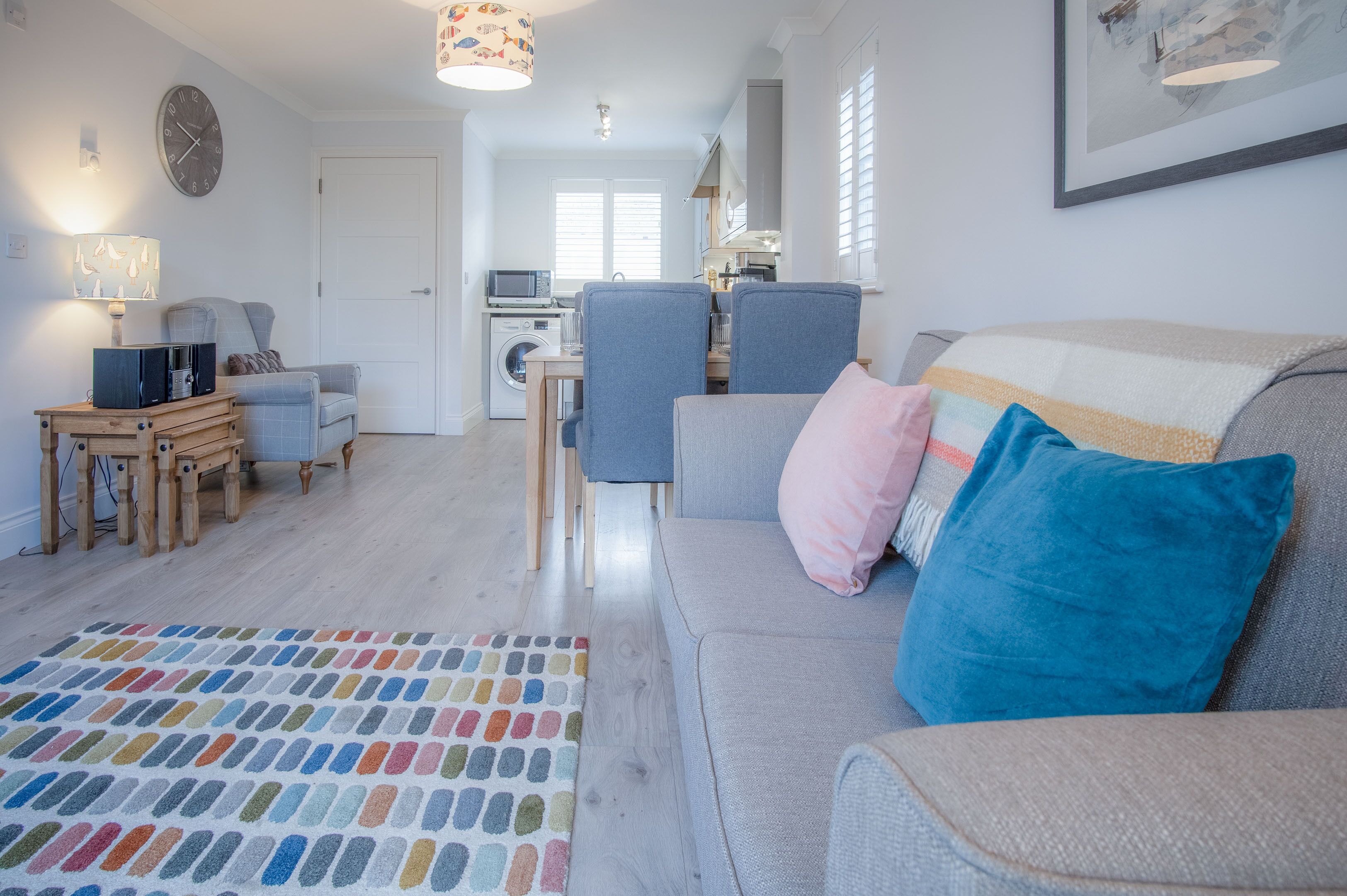 Un salon moderne avec un canapé gris, un tapis coloré et un coin repas comprenant une table et des chaises.