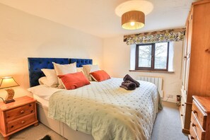 Ein Schlafzimmer mit Bett, Nachttisch, Lampe, Fenster und einem Holzschrank.
