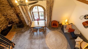 Um quarto acolhedor com parede de pedra, uma mesa de jantar, cadeiras, um sofá e uma janela grande.