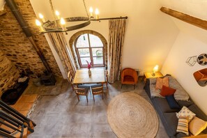 A cozy room with a stone wall, a dining table, chairs, a sofa, and a large window.