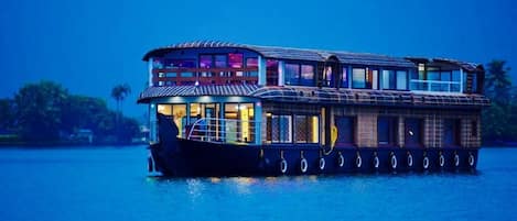 Una casa flotante con estructura de dos pisos, amplias ventanas y una cubierta techada.