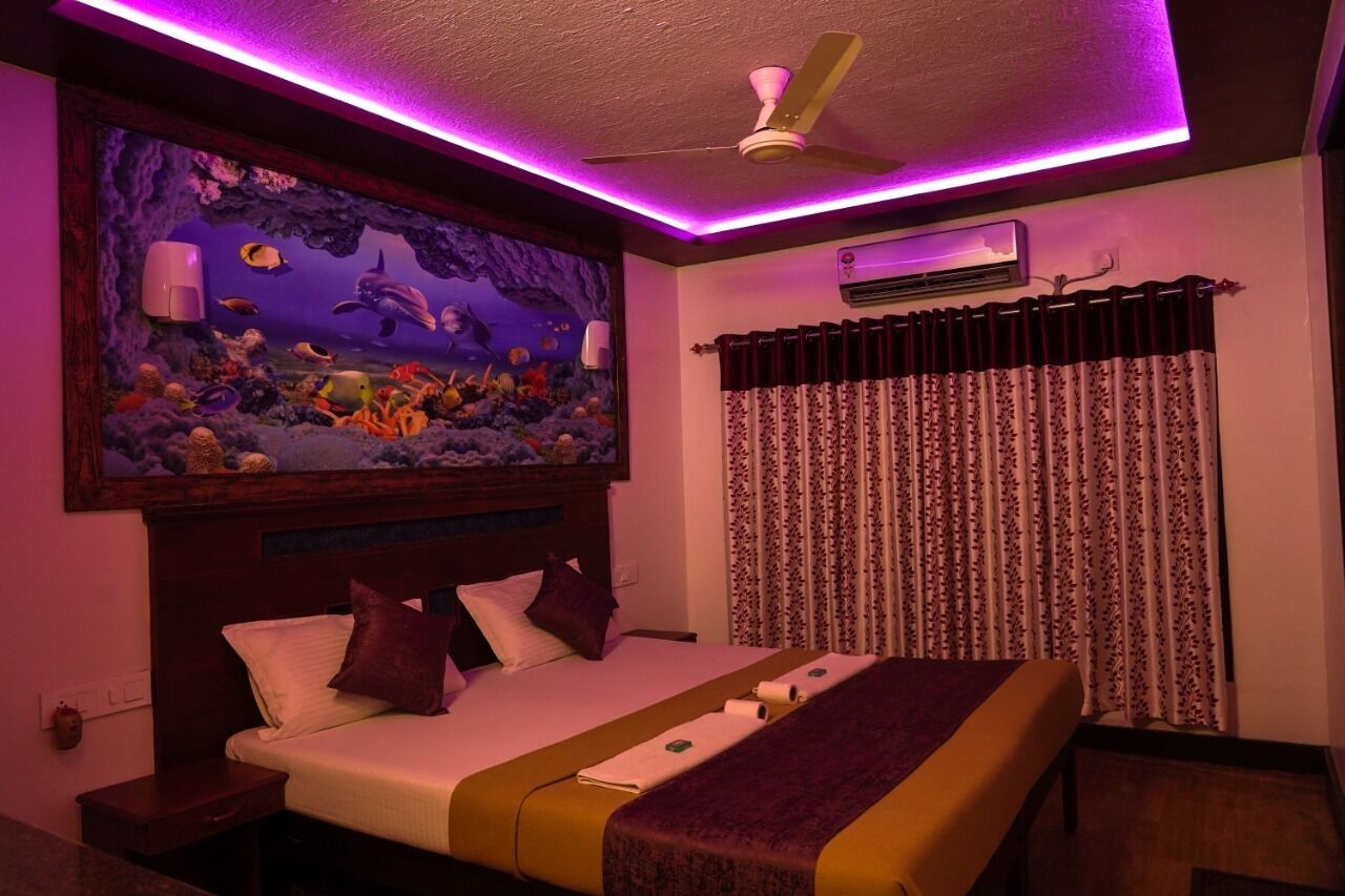 A hotel room with a bed, a ceiling fan, an air conditioning unit, and a large aquarium on the wall.