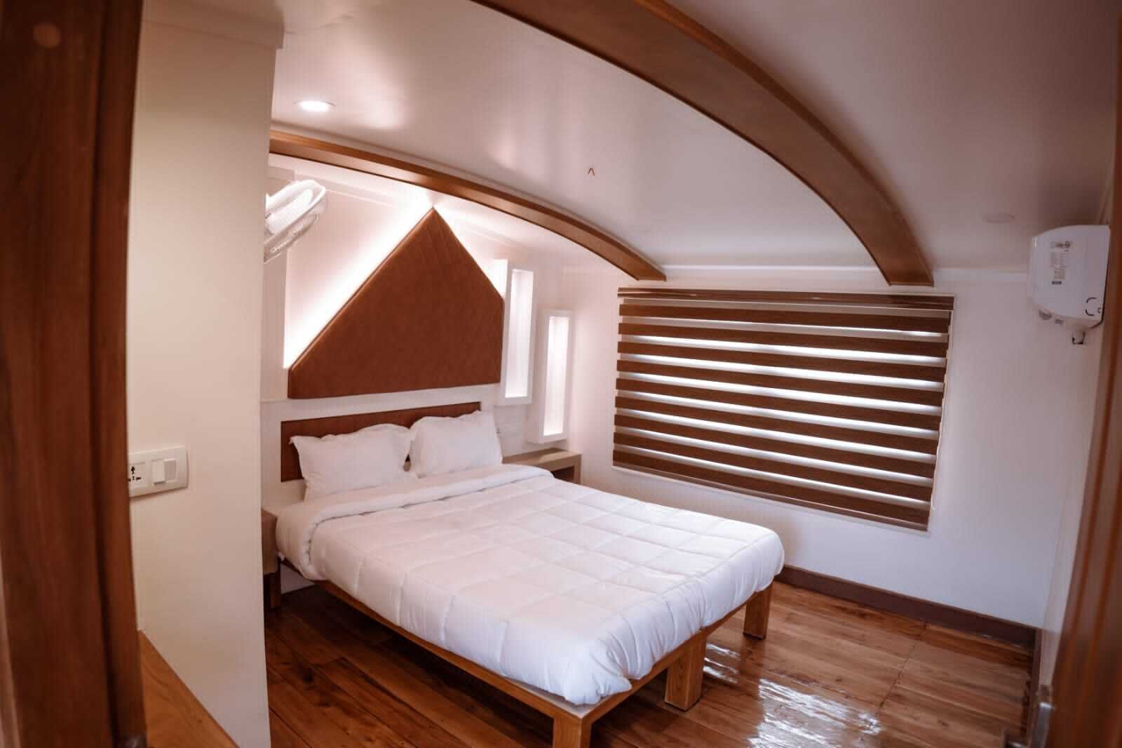 Een slaapkamer met een houten bed, wit beddengoed, een schuine balkenkap en een raam met zonwering.
