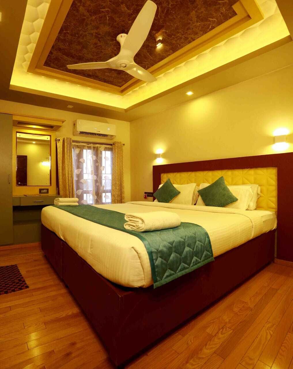 A hotel room with a large bed, a ceiling fan, an air conditioning unit, a mirror, and a window with curtains.