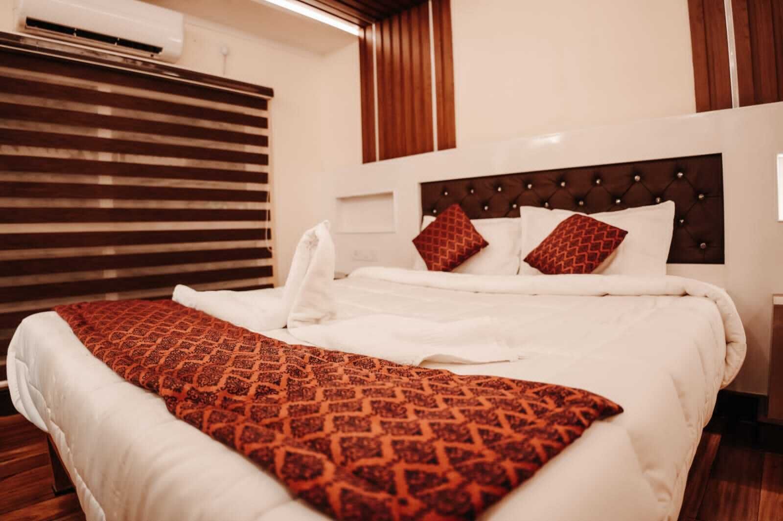 A neatly made bed with a patterned throw, a tufted headboard, and a window with blinds.