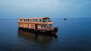 Una casa flotante grande de varios niveles con revestimiento de madera, cubierta superior protegida y un bote salvavidas visible.