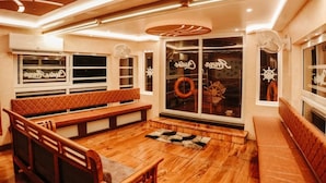 Una habitación acogedora con un banco de madera, un ventanal con vista a un barco y un techo con un diseño geométrico.