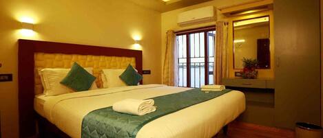 A hotel room with a large bed, a vanity with a mirror, and a window with curtains.