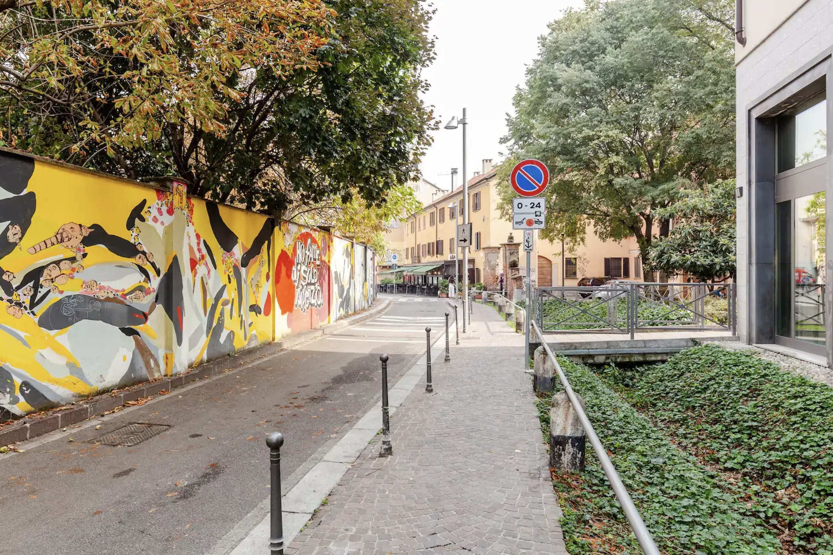 A street with a mural, a no parking sign, and a pedestrian walkway.